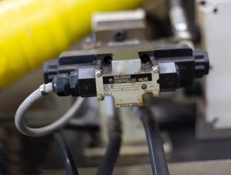 A close-up of a valve labeled Solenoid Controlled Valve in a factory. The valve contains a bit of rust.