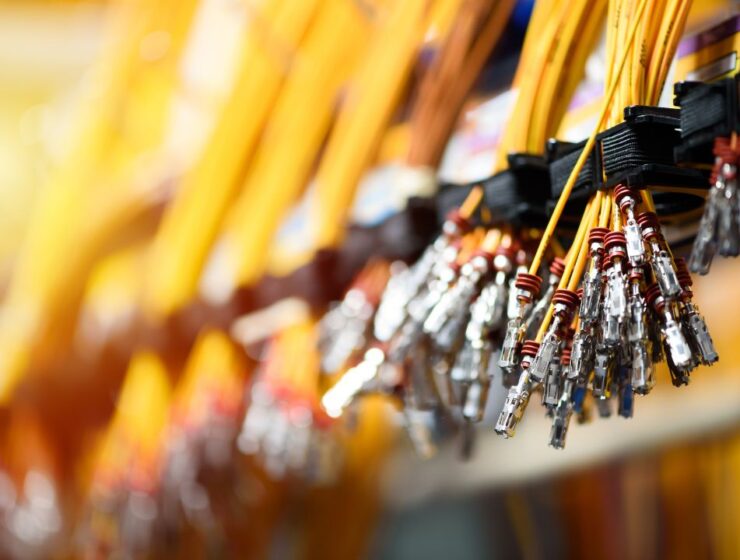 A close-up of a bundle of crimped yellow wires hanging from a mount with more wires blurred in the background.