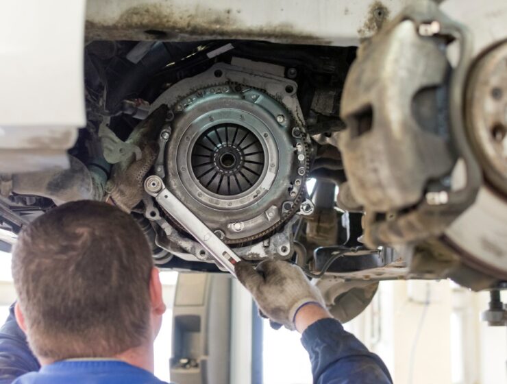 A rear view of a mechanic working on the clutch system of a vehicle elevated on a lift with a socket wrench.