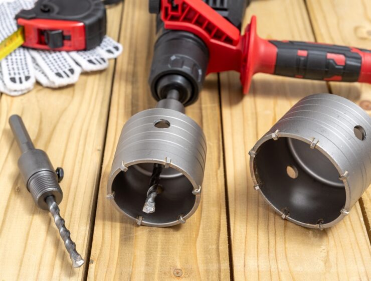 A close-up of concrete coring equipment on a wooden table, including crown drill bits and measuring tape.