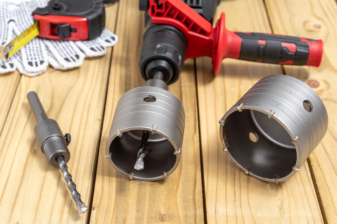 A close-up of concrete coring equipment on a wooden table, including crown drill bits and measuring tape.