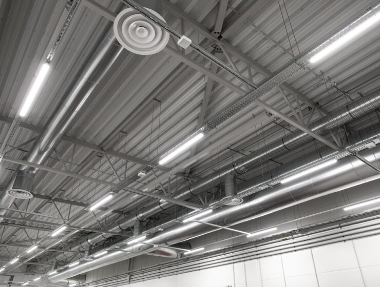 A bottom-up view of an industrial warehouse ceiling with built-in lighting arranged in rows and ductwork.