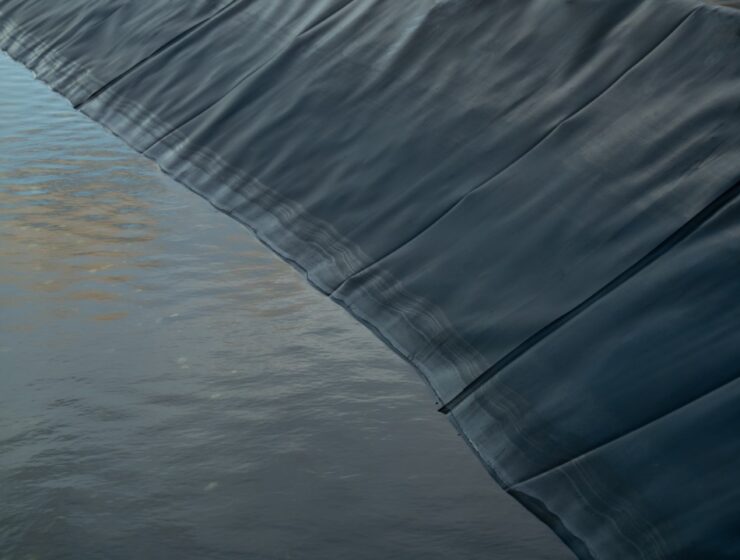 a black pond liner draping along the edge of murky water with folds and seams visible across the surface.