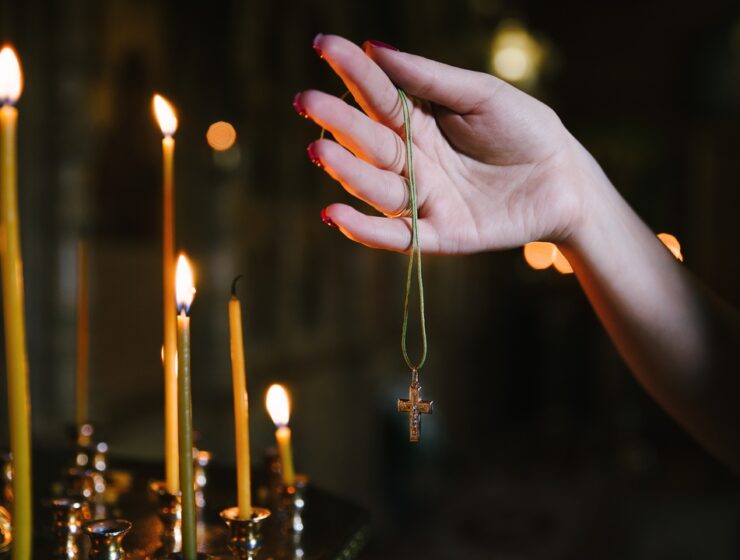 A close-up of someone holding their Rosary in their right hand near a set of taper candles burning in a dark room.