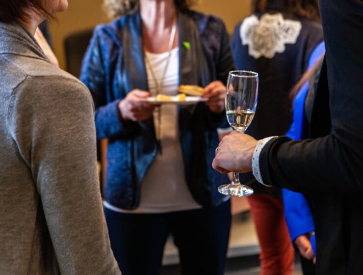 A group of adults socializes at a formal event while a man holds a champagne glass and a woman carries a plate.