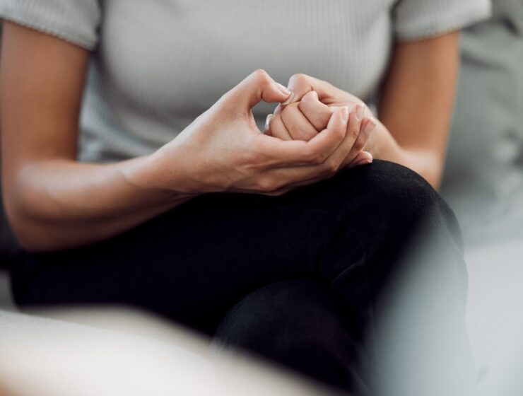 A person sits with their hands clasped together in their lap. They press their right thumb sharply on their left thumb.