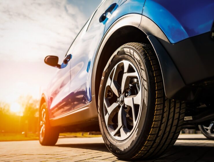 A ground-level close-up of a blue, four-door crossover with brand-new tires and wheels with the sun setting in the distance.